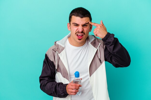 Young sporty caucasian man drinking water isolated on blue showing a disappointment gesture with forefinger.