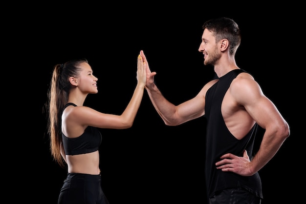 Young sporty dates smiling at each other while making high five gesture after training