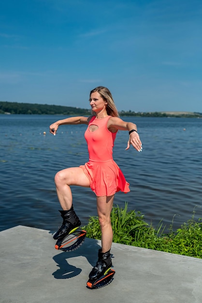 Young sporty energetic girl in a dress jumps on special shoes with springs near the lake