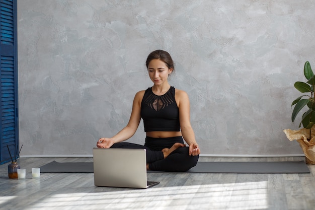 Young sporty female yoga instructor coaching online, making video of yoga lessons on laptop camera.