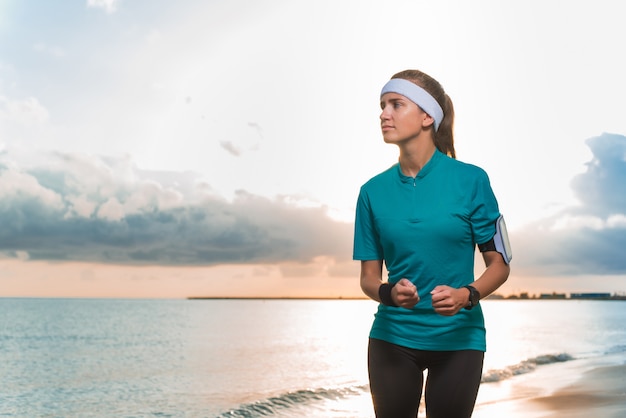 Young sporty girl running on beach at sunrise in morning