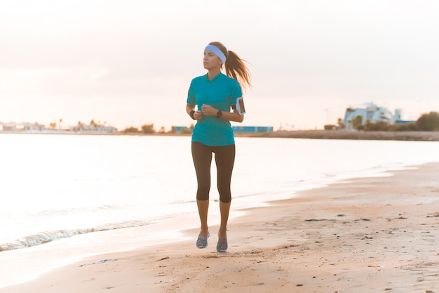 Young sporty girl running on beach at sunrise in morning