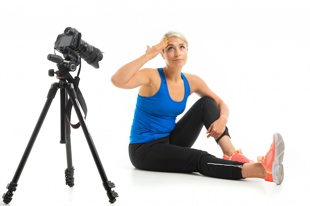 The young sporty girl with a fair hair sits in front of the camera, shows how to do exercise and she is tired
