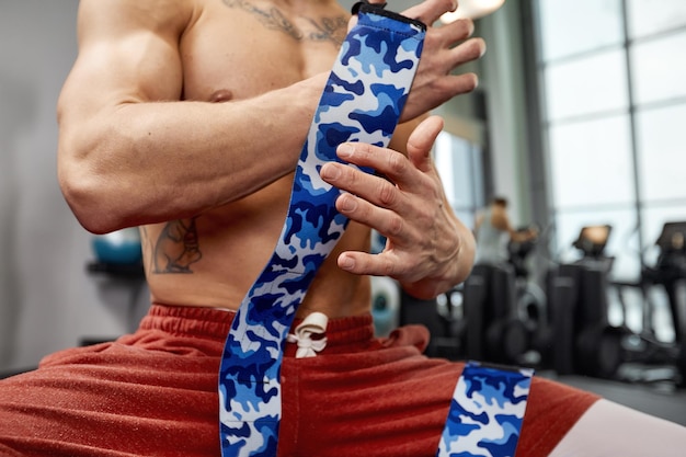 Young sporty handsome man wraps his arms with gymnastic bandage getting ready for barbell exercises