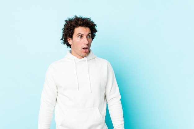 Young sporty man against a blue background being shocked because of something she has seen.