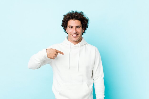 Young sporty man against a blue background person pointing by hand to a shirt copy space, proud and confident