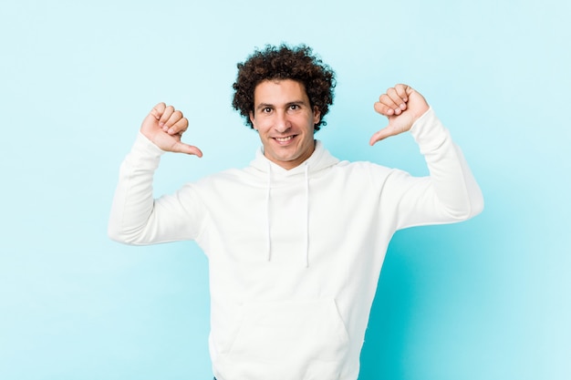 Young sporty man against a blue wall feels proud and self confident, example to follow.