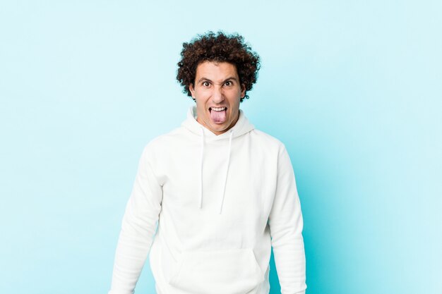 Young sporty man against a blue wall funny and friendly sticking out tongue.