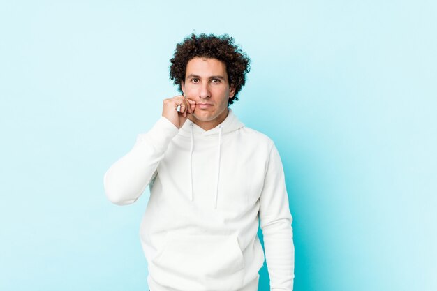 Young sporty man against a blue wall with fingers on lips keeping a secret.