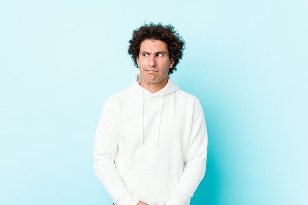 young sporty man on blue background confused, feels doubtful and unsure.
