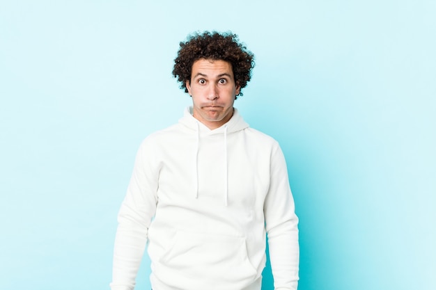 young sporty man on blue blows cheeks, has tired expression. facial expression concept.
