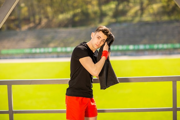 Photo young sporty man resting and wiping his sweat with a towel after workout sport exercises outdoors