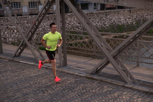 Young sporty man running on sidewalk at early morning jogging with city sunrise scene in background