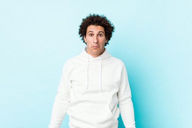 young sporty man shrugs shoulders and open eyes confused
