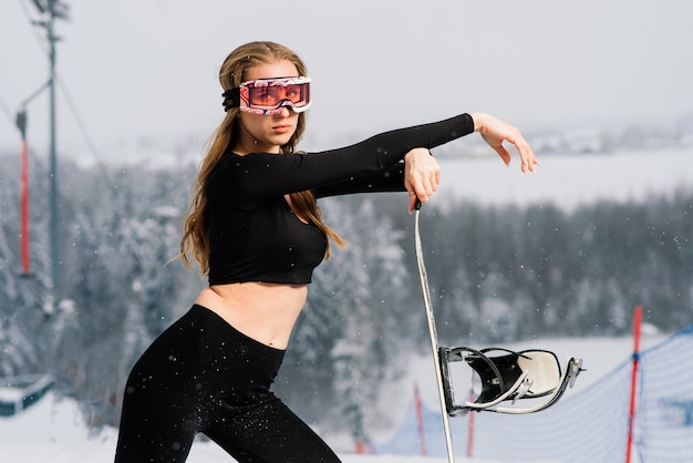 Young sporty smiling woman in winter with snowboard, glasses