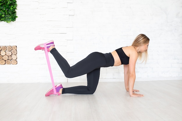 Young sporty woman doing exercises with rubber band indoor on floor