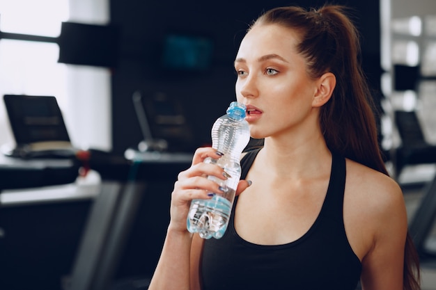 ジムで水を飲む若いスポーティな女性