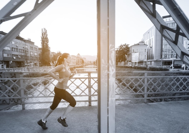 young sporty woman jogging across the bridge at sunny morning in the city