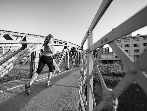 young sporty woman jogging across the bridge at sunny morning in the city