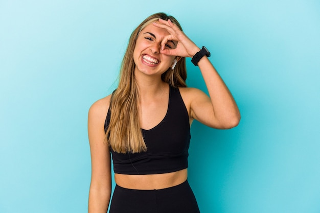 Young sporty woman listening to music with earphones isolated excited keeping ok gesture on eye.