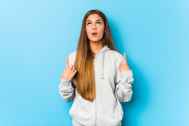 Young sporty woman pointing upside with opened mouth.