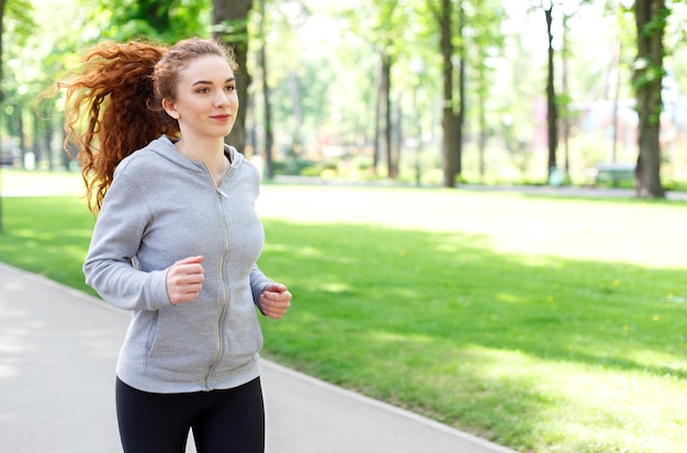 朝のトレーニング中に緑豊かな公園で走っている若いスポーティな女性、コピースペース