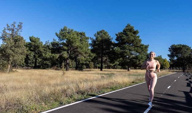 Young sporty woman running on a paved road and listening to\
music smiling athlete girl running on a road and listening to music\
concept of healthy life and woman running on the road