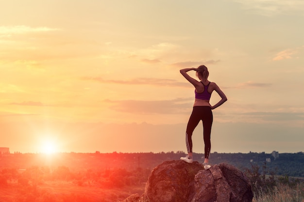 Young sporty woman with arms raised up at sunset