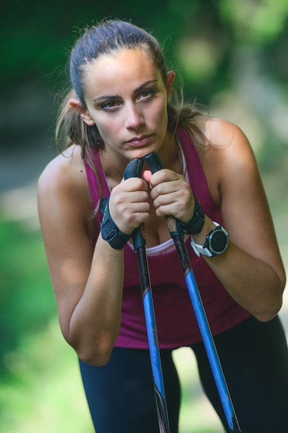 Young sporty woman with Nordic walking poles is resting