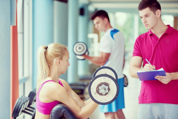 young sporty woman with trainer exercise weights lifting in fitness gym