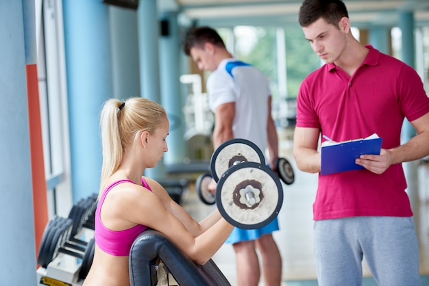 Young sporty woman with trainer exercise weights lifting in\
fitness gym