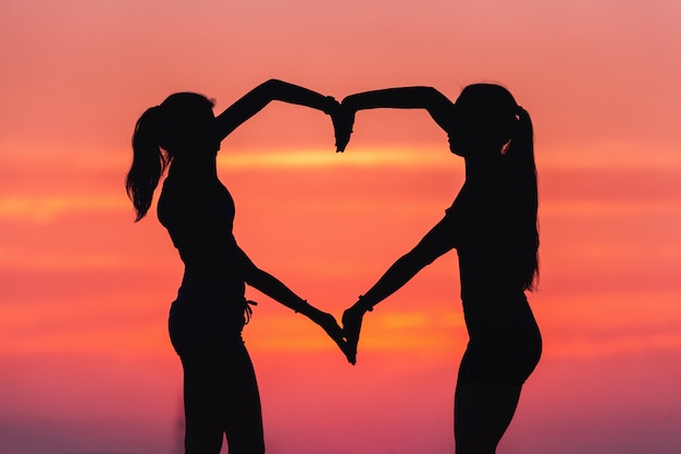 Photo young sporty women holding hands in heart shape at sunset