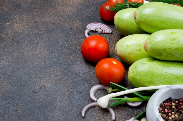 Young spring zucchini, tomatoes, herb and spices on black background