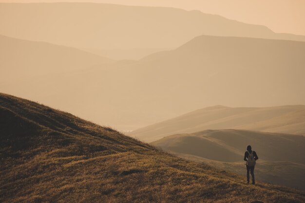 Young standing man with backpack. Hiker on the stone on the seashore at colorful sunset sky. Beautiful landscape with sporty man rocks sea and clouds at sunset. Sporty lifestyle