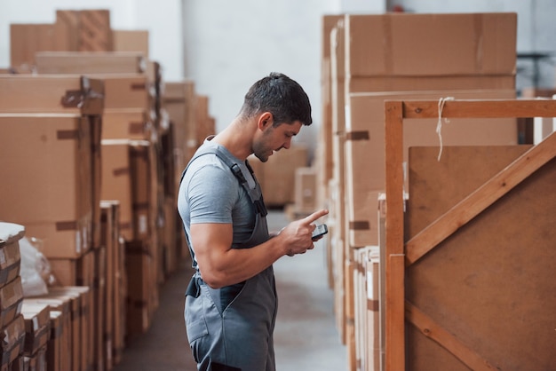 Young storage worker in uniform stands and uses his phone.