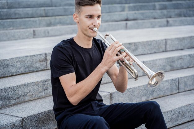 Young street musician playing guitar sitting on granite steps