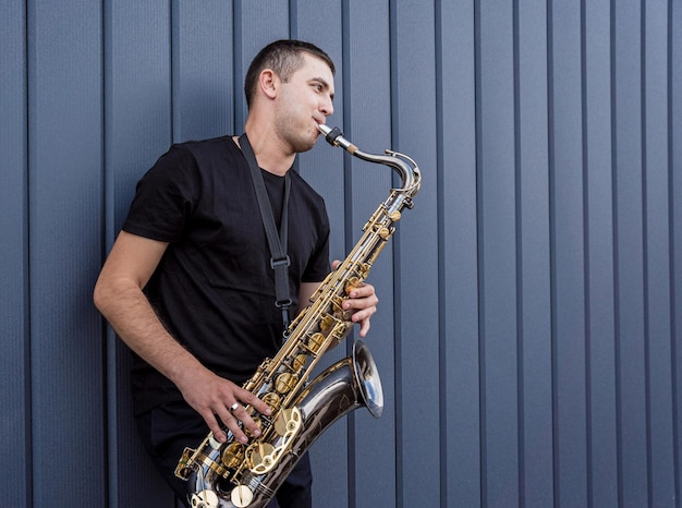 Young street musician playing saxophone near the big blue\
wall