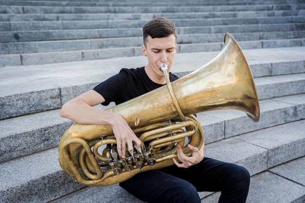 Young street musician playing tuba sitting on granite steps