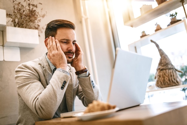 Young stressed businessman on a break in a cafe. He is working at laptop and thinking.