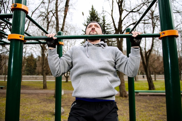 Young strong man does pull-ups on a horizontal bar on a sports ground in the summer in the city