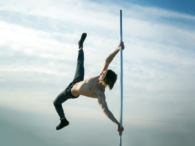 Young strong man pole dancing Pole dance sport pole dance training of young man dancer on blue sky surface