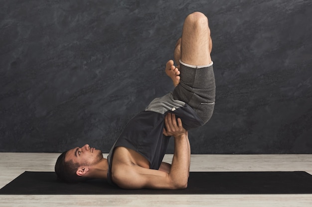 Young strong man practicing yoga, standing in flexible pose on hands on mat in fitness class, making balance exercise, copy space