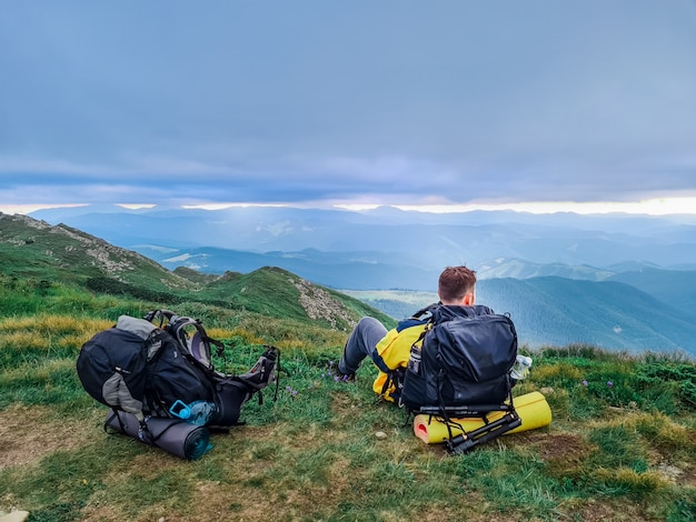 Young strong man with backpack sitting on the ground resting after climbing up. overcast weather. beauty in nature