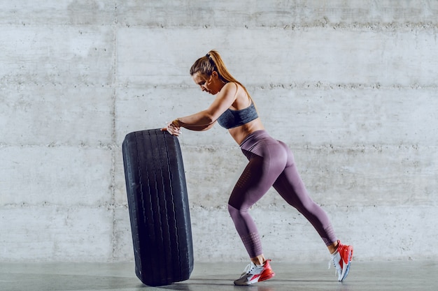 Young strong muscular caucasian sportswoman in sportswear with ponytail flipping tire. Healthy lifestyle concept.