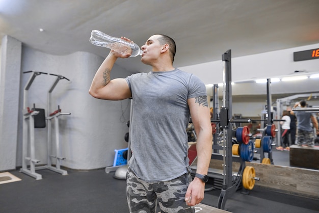 Young strong muscular man in gym drinking water from bottle