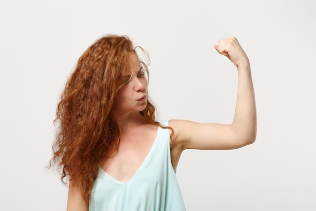 Foto ragazza giovane forte donna rossa in abiti leggeri casual in posa isolata su sfondo bianco, ritratto in studio. concetto di stile di vita di emozioni sincere della gente. mock up copia spazio. mostrando bicipiti, muscoli.