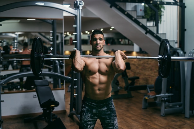 Young strong shirtless bodybuilder lifting barbells