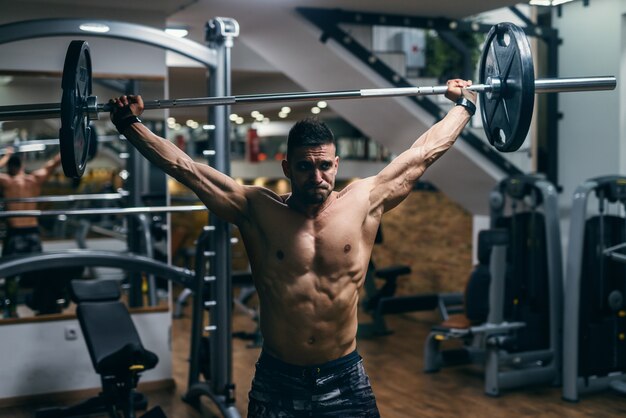 Young strong shirtless bodybuilder lifting barbells