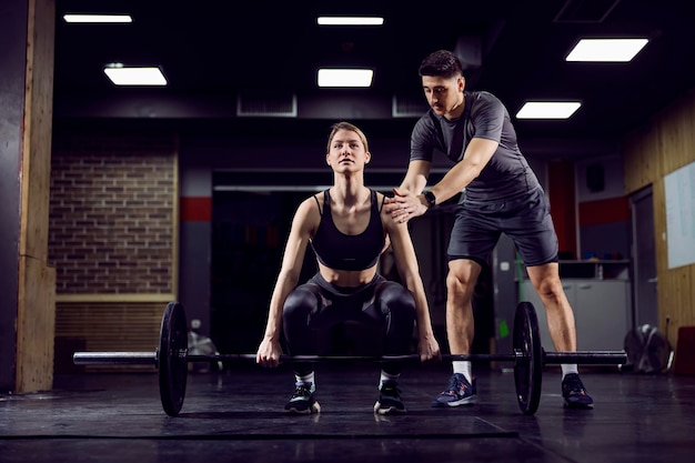 Молодая сильная спортсменка поднимает тяжести в спортзале со своим личным тренером
