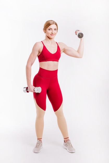 Young strong and sporty woman in red cloth doing exercises with dumbbells on white background